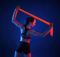 Yellow colored tape, for stretching the hands. Beautiful muscular woman is indoors in the studio with neon lighting photo