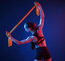 Holding stretching, tape in hands. Beautiful muscular woman is indoors in the studio with neon lighting photo