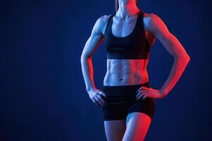Close up view of abs. Beautiful muscular woman is indoors in the studio with neon lighting photo