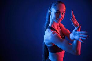 Smiling and showing muscles, on hands. Beautiful woman is indoors in the studio with neon lighting photo