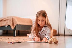 Little girl is lying down on the floor at home and drawing photo