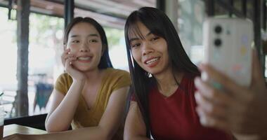 Portrait of Two Asian women are enjoying talking with a friend via call on mobile phone at a table in a coffee shop. Family enjoying time together. Happy lifestyle photo