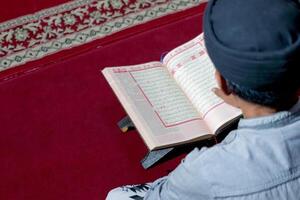Man Reading the Quran on a Red Carpet in a Peaceful Setting photo