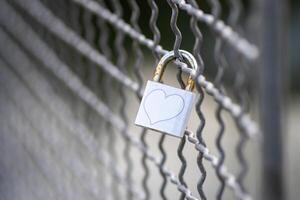 View of a gray padlock on an iron bridge fence with a painted heart photo
