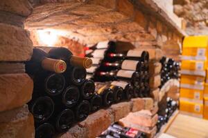 A wine cellar featuring brick shelves with wine bottles stored horizontally, warm lighting, and yellow boxes contrasting the earthy tones. photo
