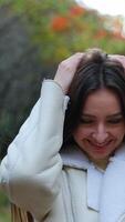 Beautiful rejoicing woman wearing white warm jacket taking a stroll by the forest. Lady warms her hands and enjoys fresh autumn air. Vertical video