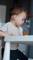Beautiful child plays with a toy standing at the table. Baby boy tries to climb on the chair. Vertical video