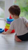 Rear view of Caucasian toddler playing with pyramid. Peaceful child assembling a pyramid on a balcony. Vertical video