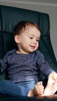 Pretty happy toddler sitting in a black office chair. Beautiful child turns to the table trying to reach something. Low angle view. Vertical video