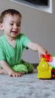 sorridente caucasiano Garoto senta em a chão jogando com brinquedo. feliz saudável criança empurra dele trem. vertical video