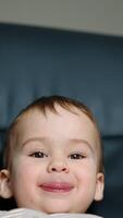 Beautiful joyful kid shows tongue to camera. Kid sits in black chair looking and speaking to camera. Close up. Vertical video