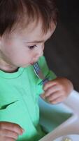 Toddler sitting at feeding table eats from fork. Mom's hand gives a spoon with porridge to her child. Top view close up. Vertical video