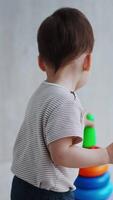 One year old toddler plays with a pyramid. Rear view of a boy disassembling the toy and then collecting again. Vertical video