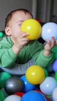 Happy smiling kid leaned on the dry pool and plays with balls. Adorable toddler playing indoors. Vertical video