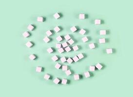 Scattered white sugar cubes on light green background in random pattern. photo