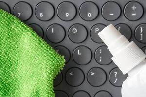 Clean keyboard with green cloth and spray bottle for effective digital hygiene on black circular keys. photo