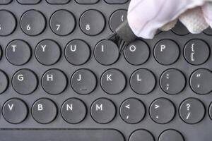 Gloved hand cleaning black computer keyboard with brush close up technology hygiene concept. photo
