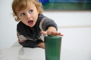 Curious Young Child Reaching for Glass with Excited Expression photo