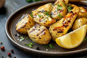 Grilled artichoke hearts with lemon wedge and herbs on dark plate served at a rustic table setting. Roasted artichoke hearts garnished with fresh herbs and accompanied by a lemon wedge, healthy snack photo