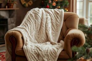 Cozy home setting with a textured blanket draped over a comfortable armchair, festive holiday decor. Soft knitted blanket rests over stylish armchair in warmly lit living space decorated for holidays photo