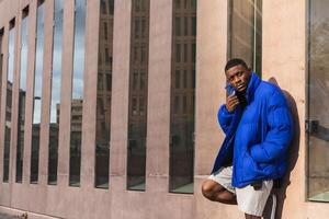 A man in a blue jacket leaning against a building photo