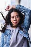A woman in a denim jacket leaning against a wall photo