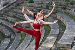 Two women in red and black outfits doing yoga on the steps of an ancient amphitheater photo