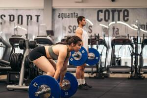 A man and woman in a gym with a barbell photo