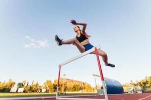 A female athlete jumping over a hurdle photo