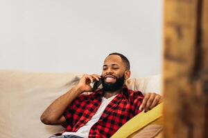 A man with a beard and checkered shirt sitting on a couch talking on his phone photo