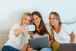 Three women sitting on a couch with laptops photo