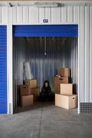 A storage unit with boxes and a man sitting in the doorway photo