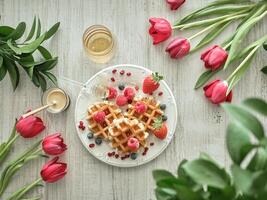 Waffles with berries and honey on a white table with red tulips and red roses photo