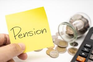 PENSION text on sticky note with Calculator. Thai Baht Coins spilled out of jar glass isolated on white background, Retirement concept. photo