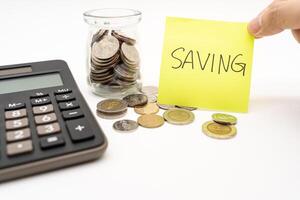 Saving money concept with SAVING text on sticky note. Commitment to achieving financial goals. isolated on white background. Thai Baht Coins spilled out with Calculator. photo