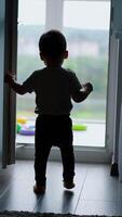 Little baby runs up to a balcony door and closes it. Then opens again and walks happily to a balcony. Vertical video