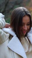 Cheerful positive lady puts on warm jacket walking in the park. Woman looks into camera smiling posing at the backdrop of beautiful autumn weather. Vertical video