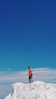 Muscular man on white hill. Bodybuilder without shirt posing on the top of the mountain under blue sky. Motion camera back. Vertical video