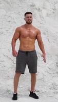Bearded man with muscular body poses on white mountain background. Strong bodybuilder outdoors in summer. Vertical video