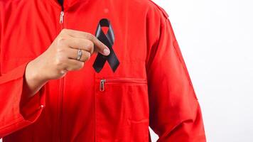 Hand of man holding black ribbon on his chest as symbol of mourning and melanoma cancer awareness isolated on white background photo
