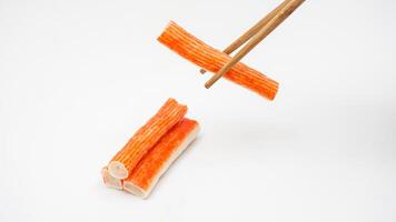 Uncooked crab stick or imitation crab meat made from processed fish meat picked up with chopsticks isolated on white background photo