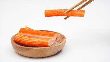 Crab stick or imitation crab meat made from processed fish meat on wooden plate and picked up with chopsticks isolated on white background photo