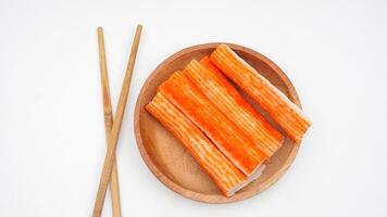 Crab stick or imitation crab meat made from processed fish meat on wooden plate with chopsticks isolated on white background photo