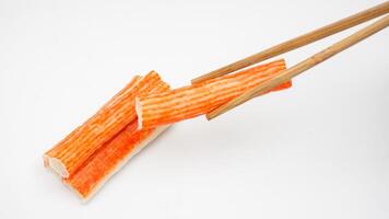 Crab stick or imitation crab meat made from processed fish meat picked up using chopsticks isolated on white background photo