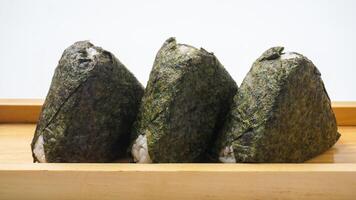 Three onigiri or Japanese rice ball in triangle shaped wrapped with nori or dried seaweed on wooden coaster isolated on white background photo