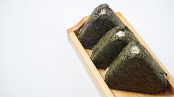 Three delicious onigiri or Japanese savory rice ball wrapped in nori dried seaweed on wooden coaster isolated on white background photo