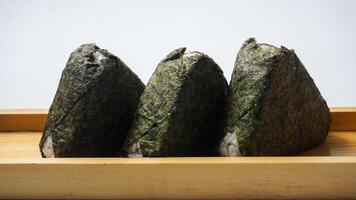 Three onigiri or Japanese rice ball wrapped in nori dried seaweed on wooden coaster isolated on white background photo