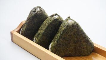 Three delicious onigiri or Japanese rice ball wrapped in nori dried seaweed on wooden coaster isolated on white background photo
