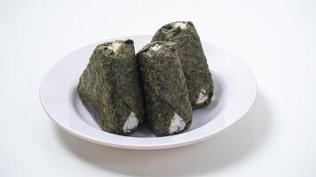 Three onigiri or Japanese rice ball in triangle shaped wrapped with nori or dried seaweed on plate isolated on white background photo