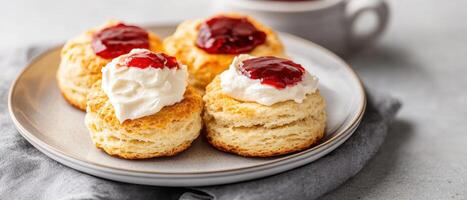 Homemade scones topped with clotted cream and jam on plate, perfect for tea time. Enjoy delightful combination of flavors and textures in this classic treat photo